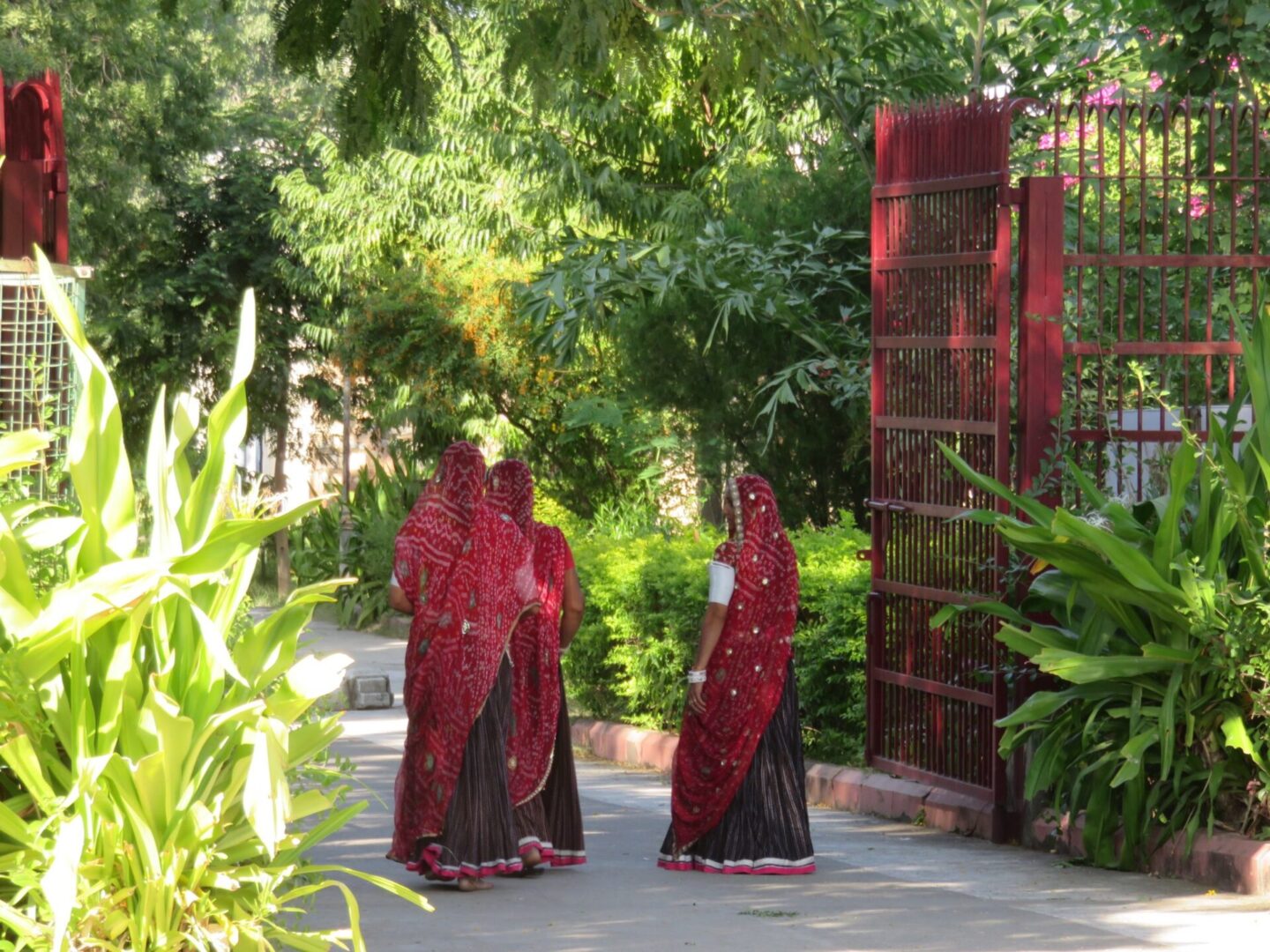 Two women in red and black dresses standing next to a gate.